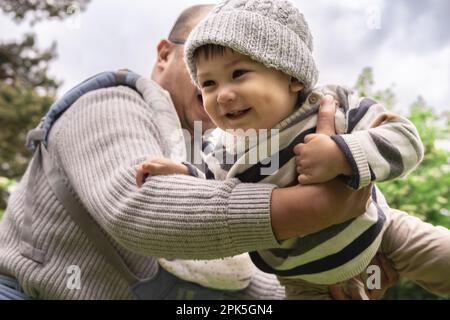 Neuer Vater spielt mit süßem Baby, hebt, wirft ein süßes Baby in die Luft, hält das Kind mit Liebe in Armen, genießt Vaterschaft, Elternschaft. Kindergröße Stockfoto