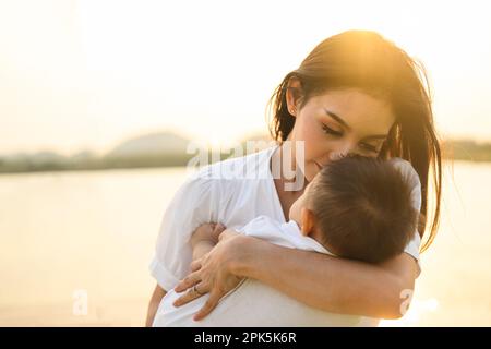 Liebevolle Mutter hält und trägt ihr Neugeborenes in einem öffentlichen Park Stockfoto