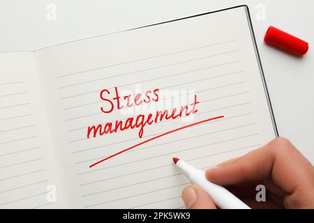 Mann schreibt Wörter Stress Management in Notizbuch auf weißem Hintergrund, Draufsicht Stockfoto