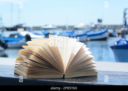 Offenes Buch auf einer Holzbank in der Nähe des Meeres Stockfoto