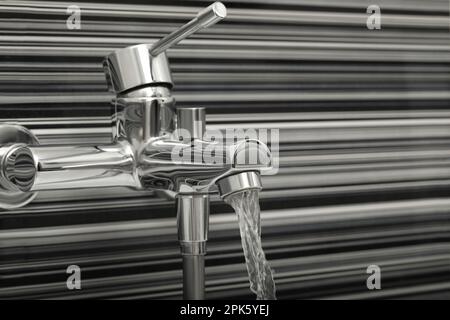 Wasser fließt aus dem Wasserhahn, der an den schwarzen und weißen Wänden installiert ist Stockfoto