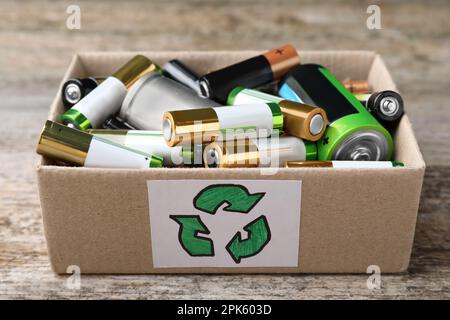 Gebrauchte Batterien in einem Karton mit Recycling-Symbol auf dem Holztisch, Nahaufnahme Stockfoto