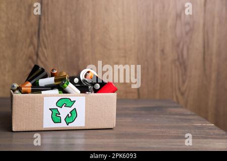 Gebrauchte elektrische Batterien in einem Karton mit Recycling-Symbol auf dem Holztisch. Platz für Text Stockfoto