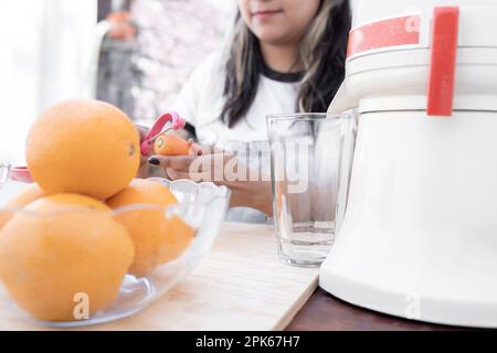 Eine junge Hispanoamerikanerin schält Karotten, um Orangen- und Karottensaft mit einer alten Pressvorrichtung herzustellen Stockfoto