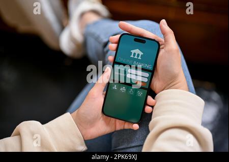 Chiang Mai, Thailand - April 05 2023: Nahaufnahme einer Frau in legerer Kleidung, die ihre mobile Banking-App auf ihrem Smartphone nutzt, während sie sich in einem Café entspannt. Stockfoto