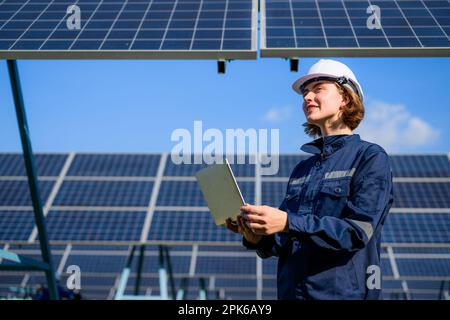 Eine Ingenieurin, die einen Laptop hält und Solarmodule auf einer Solarzellenfarm überprüft Stockfoto