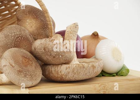 Shiitake-Pilze und verschiedene Zwiebelsorten auf einem Holzschneidbrett auf weißem Hintergrund. Rezepte und Heilkräuter Stockfoto