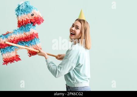 Junge Frau bricht mexikanische Pinata auf grünem Hintergrund Stockfoto