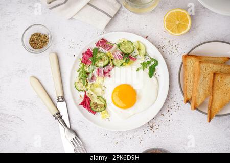 Teller mit leckerem Spiegelei, Toast und Salat auf einem hellen Tisch Stockfoto