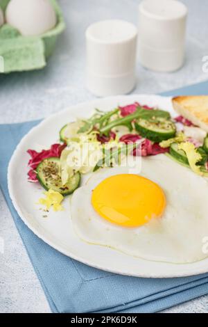 Teller mit leckerem Spiegelei, Toast und Salat auf einem hellen Tisch Stockfoto