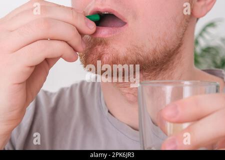 Ein weißer Mann, der eine Pille nimmt und ein Glas Wasser trinkt. Junger Mann unter Vitamineinfluss. Gesundheit, Medizin, Behandlungskonzept. Stockfoto