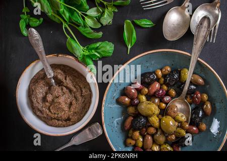 Tisch serviert mit Tapenade, gemischten marinierten Oliven (grün) (schwarz und violett) in Keramikschüssel und Basilikumblättern. Vorspeisen aus der französischen provence und Stockfoto