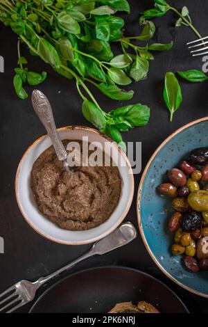 Tisch serviert mit Tapenade, gemischten marinierten Oliven (grün) (schwarz und violett) in Keramikschüssel und Basilikumblättern. Vorspeisen aus der französischen provence und Stockfoto