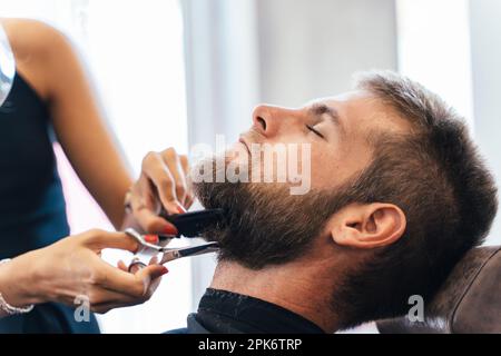 Ein unbekannter Friseur schneidet einem Mann in einem Salon den Bart Stockfoto