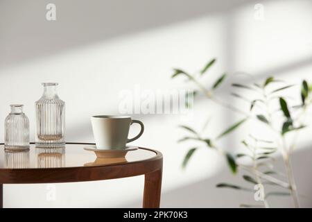 Dieser Raum bietet eine ruhige Atmosphäre mit Tageslicht. Auf dem Tisch befinden sich Tontöpfe, Glasflaschen, Kaffee und verschiedene Gegenstände. Stockfoto