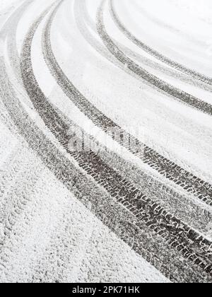 Frischer, unberührter Schnee deckt die winterliche Straße. Reifenspuren bilden ein Muster von umherziehenden Linien auf dem kristallweißen Parkplatz. Stockfoto