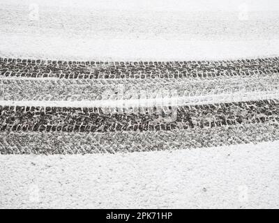 Frischer, unberührter Schnee deckt die winterliche Straße. Reifenspuren bilden ein Muster von umherziehenden Linien auf dem kristallweißen Parkplatz. Stockfoto