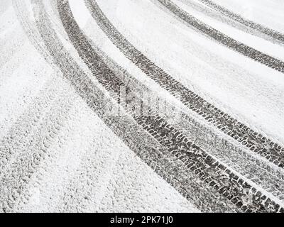 Frischer, unberührter Schnee deckt die winterliche Straße. Reifenspuren bilden ein Muster von umherziehenden Linien auf dem kristallweißen Parkplatz. Stockfoto