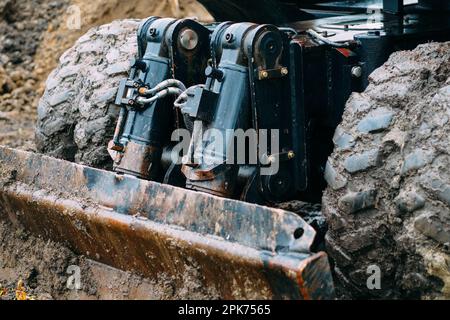 Radtraktor mit Schaufel räumt an bewölkten Regentagen den Boden frei. Schmutzige Bulldozer-Schaufel Nahaufnahme... Stockfoto