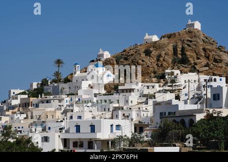 Panoramablick auf eine Kirche, kleinere Kapellen und die griechische Flagge auf einem Hügel mit Blick auf die Ägäis in iOS in Griechenland, auch bekannt als Chora Stockfoto