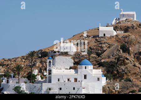 Panoramablick auf eine Kirche, kleinere Kapellen und die griechische Flagge auf einem Hügel mit Blick auf die Ägäis in iOS in Griechenland, auch bekannt als Chora Stockfoto