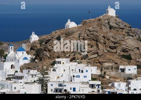 Panoramablick auf eine Kirche, kleinere Kapellen und die griechische Flagge auf einem Hügel mit Blick auf die Ägäis in iOS in Griechenland, auch bekannt als Chora Stockfoto