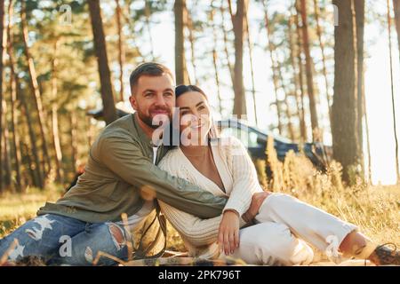 Sich gegenseitig umarmen. Glückliches Paar, das im Wald auf dem Boden saß Stockfoto