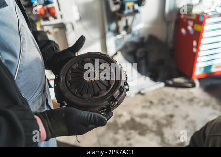 Nahaufnahme der Hände eines Mechanikers, der eine alte kaputte Kupplung in der Werkstatt hält, Reparaturkonzept. Hochwertiges Foto Stockfoto