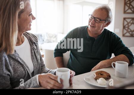 Kaffee und Unterhaltung, der beste Start in den Tag. Ein reifes Paar, das an einem entspannten Tag zu Hause Kaffee und einen Snack zusammen isst. Stockfoto