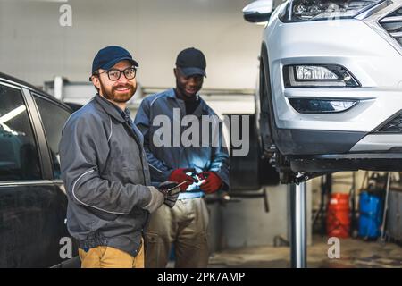 Zwei zufriedene Mechaniker, die in der Werkstatt arbeiten und lächeln, lieben Ihre Arbeit. Hochwertiges Foto Stockfoto