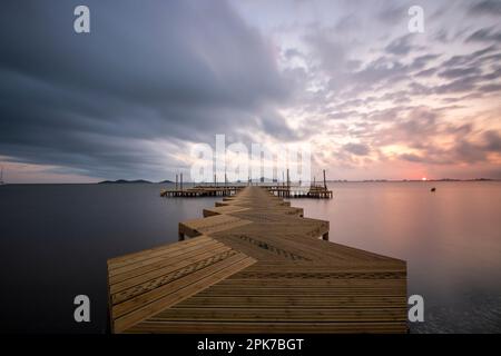 Holzsteg am Strand von Carmol im Mar Menor, bei einem bewölkten Sonnenaufgang, in Cartagena, Region Murcia, Spanien Stockfoto