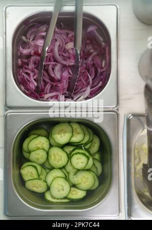 Geschnittene frische Gurken und rote Zwiebeln in Behältern, direkt von oben auf einer Küchentheke geschossen Stockfoto