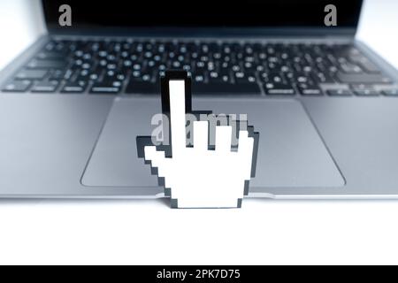 Großer, pixelartiger, handgeformter Cursor vor einem modernen Laptop. Technologiebezogenes Konzept. Stockfoto