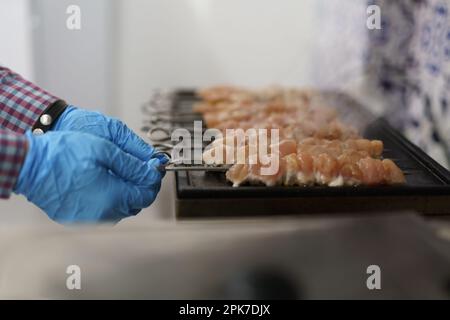 Kochen Sie Schweinefleisch auf Spießen auf einem Grill in einer kommerziellen Küche. Männlicher Mann, der in einem Fast-Food-Restaurant Fleischfilet auf einer heißen Eisentopf kocht Stockfoto