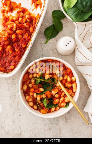 Gesundes Frühstück und Mittagessen, gedünstete weiße Bohnen mit Karotten, Zwiebeln und Tomaten mit Spinatblättern, eine Schüssel Bohnen und Spinat Stockfoto