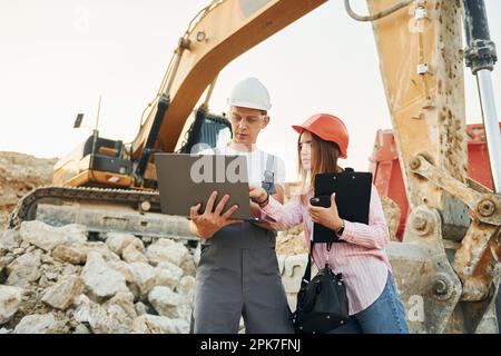Laptop verwenden. Zwei Arbeiter sind tagsüber zusammen in der Leihgrube Stockfoto