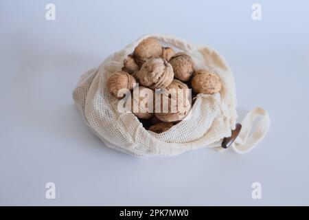 Walnüsse ohne Schale, ein Haufen Walnüsse mit Schale in drei weißen Stoffsäcken auf weißem Hintergrund nebeneinander. Stoffbeutel voller Walnüsse mit Schale. Stockfoto