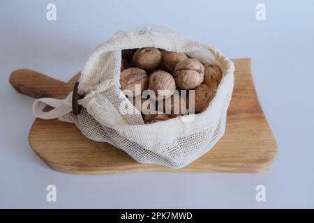 Walnüsse ohne Schale, ein Haufen Walnüsse mit Schale in weißen Stoffsäcken auf weißem Hintergrund und einem Holzschneidbrett. Stockfoto