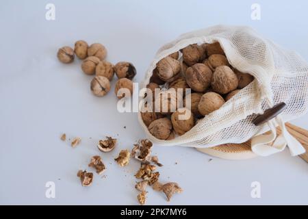 Walnusskerne, Walnussschalen und ein weißer Stoffbeutel voller Walnüsse auf einem weißen Tisch mit einem Schneidbrett. Gebrochene Walnüsse Konzeptfoto. Stockfoto