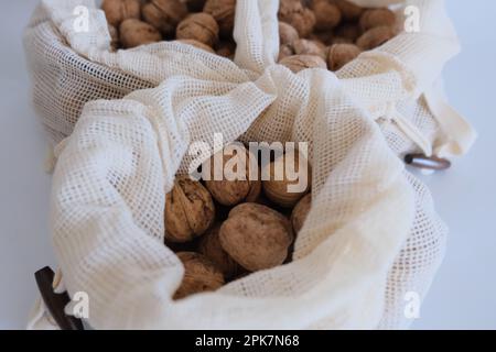 Walnüsse ohne Schale, ein Haufen Walnüsse mit Schale in drei weißen Stoffsäcken auf weißem Hintergrund. Stoffbeutel voller Walnüsse mit Schale Konzept Fotoidee. Stockfoto