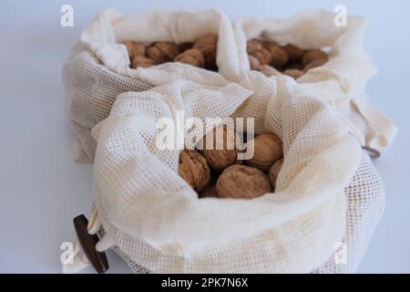 Walnüsse ohne Schale, ein Haufen Walnüsse mit Schale in drei weißen Stoffsäcken auf weißem Hintergrund. Stoffbeutel voller Walnüsse mit Schale Konzept Fotoidee. Stockfoto