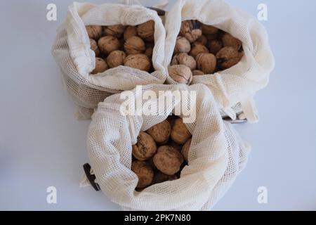 Walnüsse ohne Schale, ein Haufen Walnüsse mit Schale in drei weißen Stoffsäcken auf weißem Hintergrund. Stoffbeutel voller Walnüsse mit Schale Konzept Fotoidee. Stockfoto