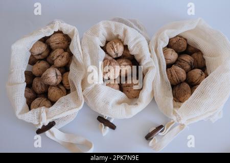 Walnüsse ohne Schale, ein Haufen Walnüsse mit Schale in drei weißen Stoffsäcken auf weißem Hintergrund nebeneinander. Stoffbeutel voller Walnüsse mit Schale. Stockfoto