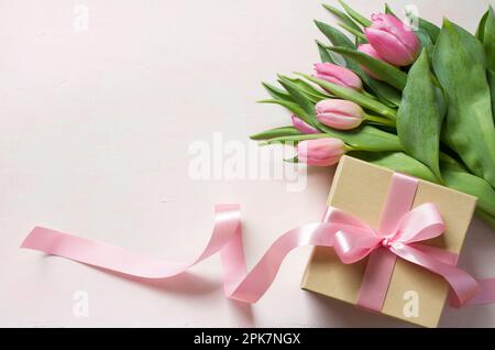 Geschenkbox mit langem pinkfarbenem Band und Tulpen auf hellem Hintergrund Stockfoto
