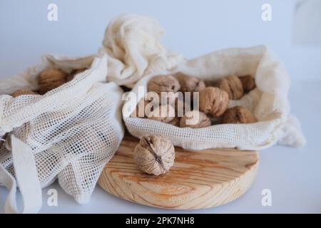 Walnüsse ohne Schale, ein Haufen Walnüsse mit Schale in weißen Stoffsäcken auf weißem Hintergrund und einem Holzschneidbrett. Stoffbeutel voller geschälter Walnüsse. Stockfoto