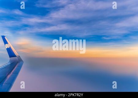 Blick auf einen Flugzeugflügel und den bunten/bunten Himmel mit verstreuten Wolken, während die Dämmerung über dem Himalaya bricht Stockfoto