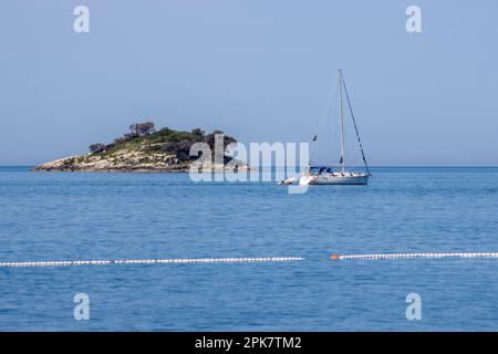 ROVINJ, KROATIEN - 15. MAI 2022 Vergnügungsyacht, vorbei an einer kleinen Insel in der Adria mit einer Linie aus rot-weißen Bojen Stockfoto