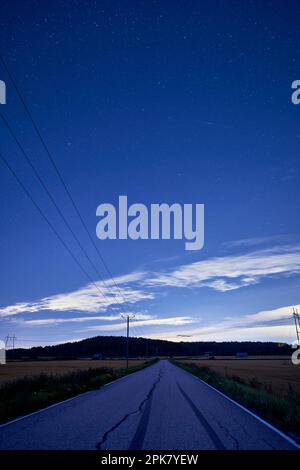 Ein langer, einsamer Abschnitt der Autobahn mit hohen Stromleitungen, die parallel dazu verlaufen Stockfoto