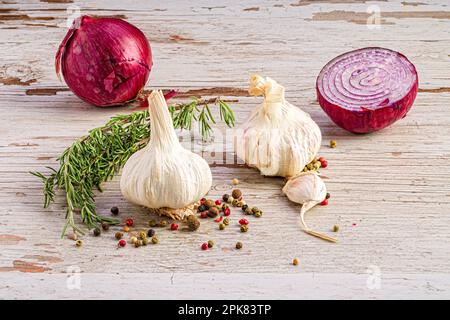 Eine Nahaufnahme von Knoblauch und Zwiebelköpfen neben einem Rosmarin-Zweig Stockfoto