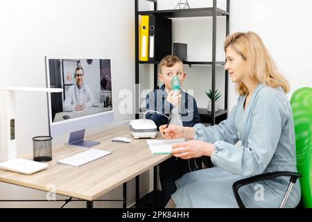 Kaukasischer kleiner Junge, der zu Hause mit einem Vernebler inhaliert. Eine junge Mutter, die ihrem Sohn beim Einatmen mit einem Vernebler hilft, bei einem Online-Meeting mit einem D. Stockfoto